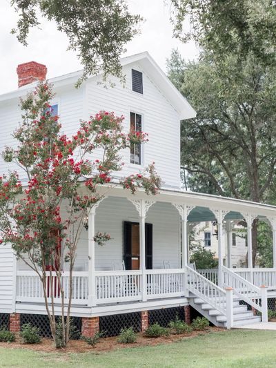 White two-story house with a porch and flowering tree in front.