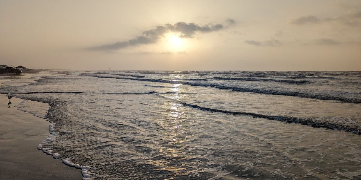 Sunset over a calm sea with gentle waves on the shore.