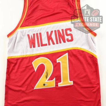 Red basketball jersey with 'WILKINS' and number 21, signed, displayed on a white and red background.