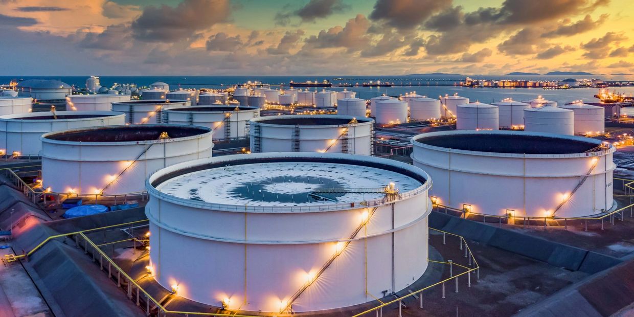Large industrial oil storage tanks at sunset with lights on.