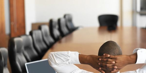 Man relaxing in a conference room with a laptop on the table.