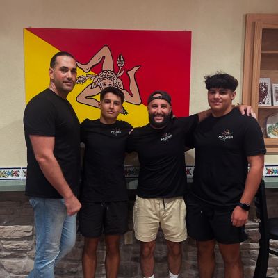 Four men posing in front of a Sicilian flag indoors.