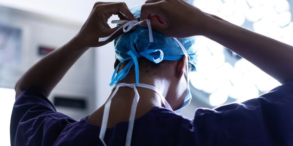 A photograph of a surgeon tying on a surgical mask.