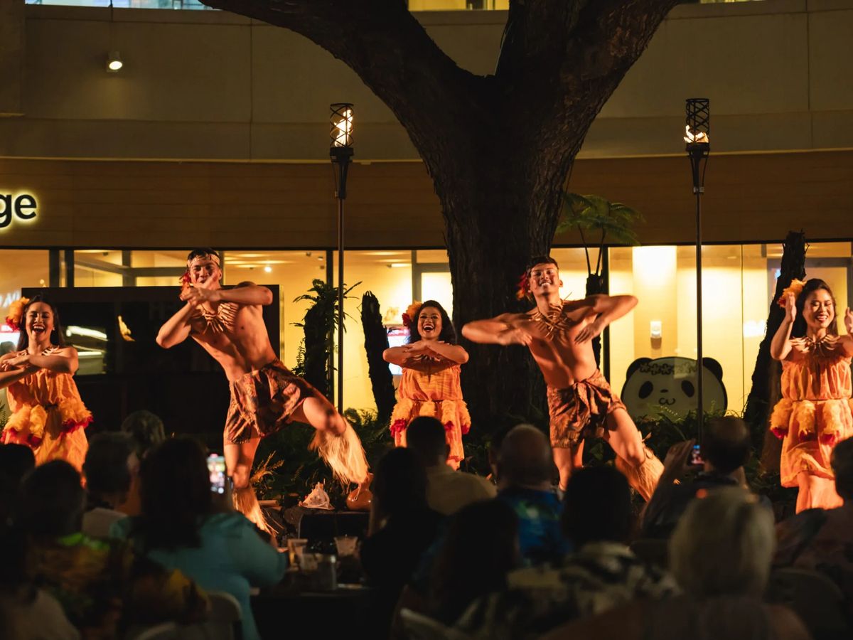 Guests watching Queens Waikiki Luau dancers beneath the courtyard tree