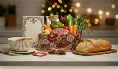A festive holiday gift basket with fresh vegetables, bread, and a bowl of soup on a table.