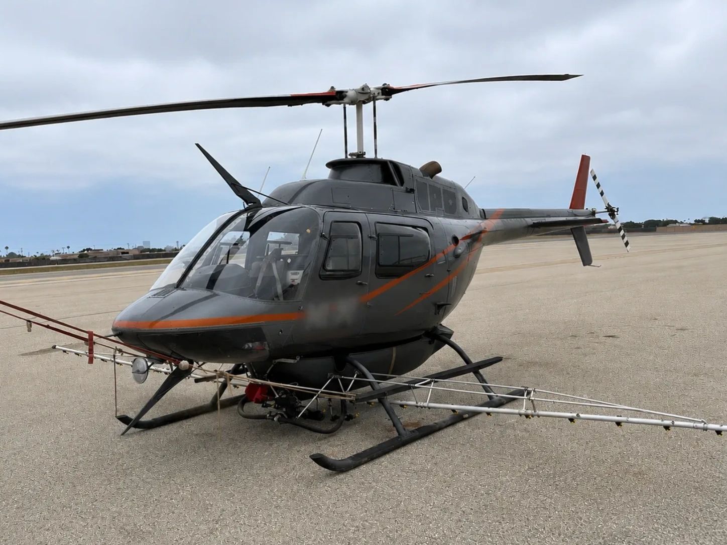 Gray helicopter on an airstrip under a cloudy sky.