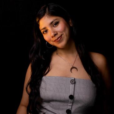Young woman with long dark hair smiling against a black background.