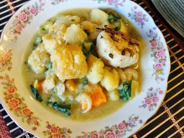 A plate of vegetable stew with dumplings and greens.