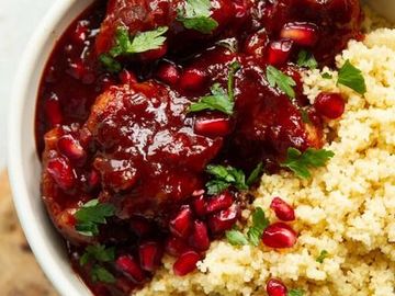 Bowl of rich stew with pomegranate seeds and couscous.