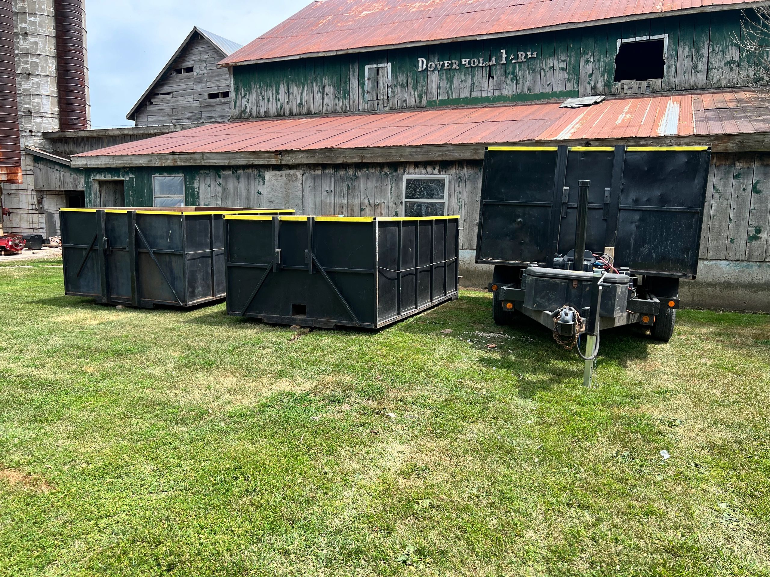 Black metal containers and trailer in front of a rustic barn.