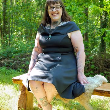 Smiling woman in black dress sitting on wooden bench outdoors.