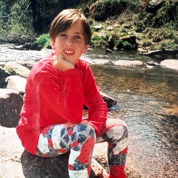 Child smiling by a stream wearing colorful clothes.