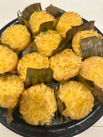 Cheesy yellow cupcakes wrapped in banana leaves on a black plate.