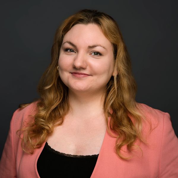 Woman with wavy hair in a coral blazer smiling.