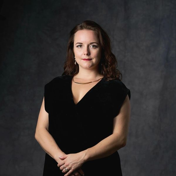 Confident woman in a black dress posing against a dark backdrop.