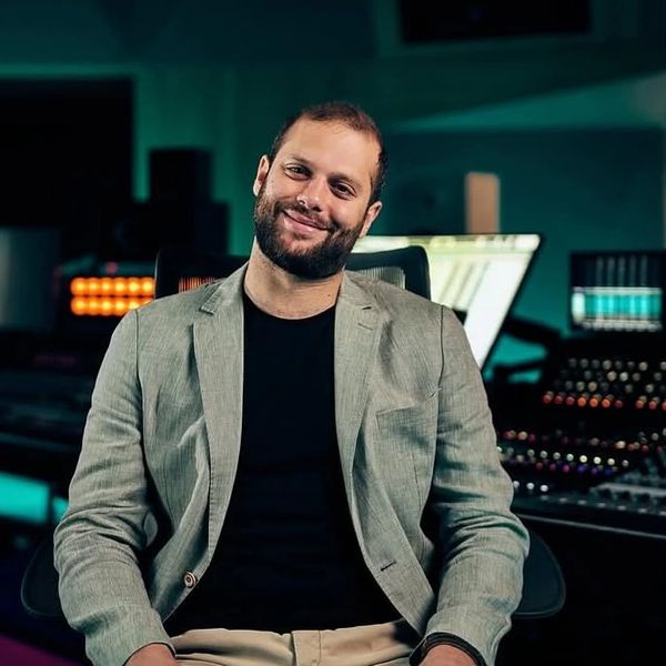 Man smiling in a recording studio wearing a blazer.