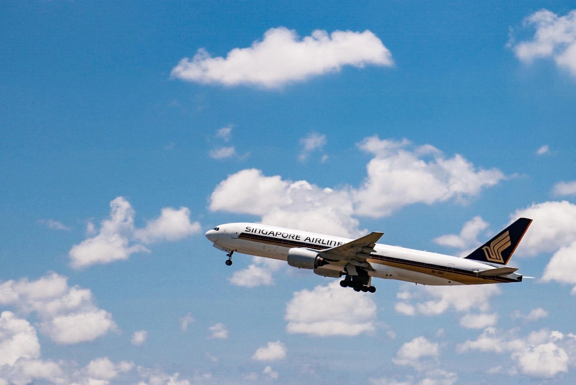 Singapore Airlines plane ascending against a blue sky with clouds.