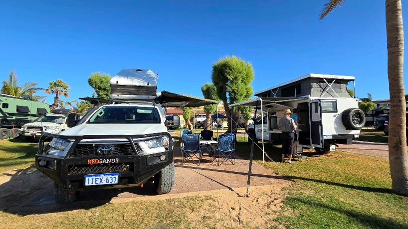 Two off-road vehicles set up with awnings and camping chairs under a clear blue sky.