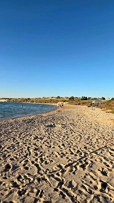 Sandy beach with clear blue sky and calm sea, few people walking and relaxing.