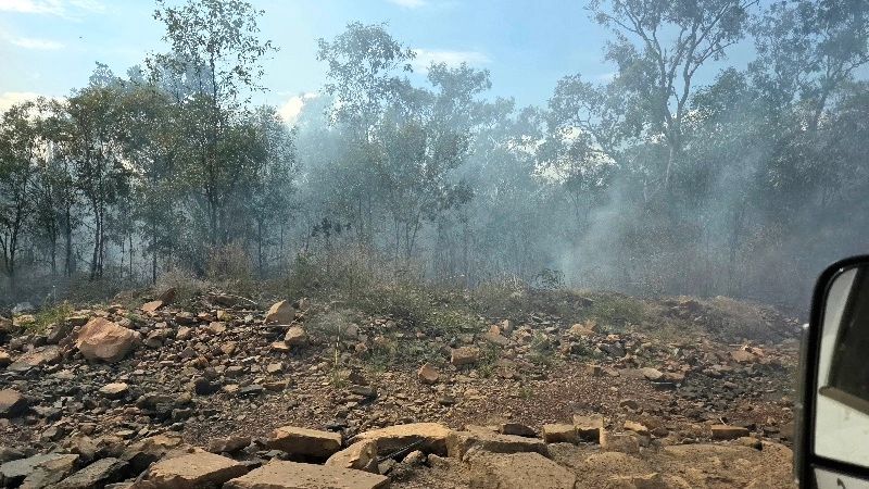 Smoke rising from a rocky forest area with sparse trees.