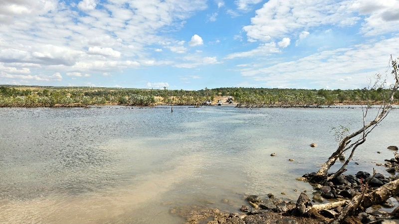 A calm river with a rocky shore and a partly cloudy sky.