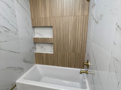 Bathroom tile installation with marble-look walls, a wood-look accent wall, recessed niches, and gol