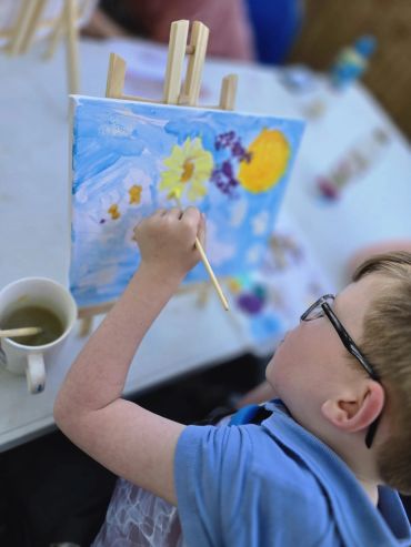 Child painting a bright flower scene on canvas.