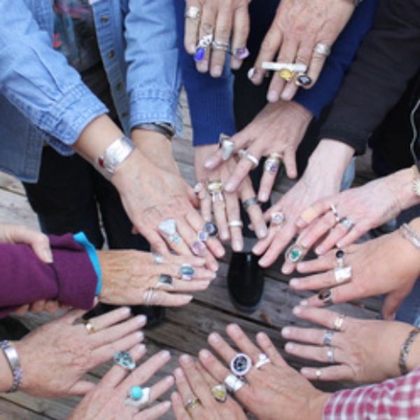 A group of hands wearing various rings arranged in a circle.