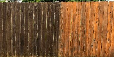A wooden fence with one side dark and the other side freshly stained.