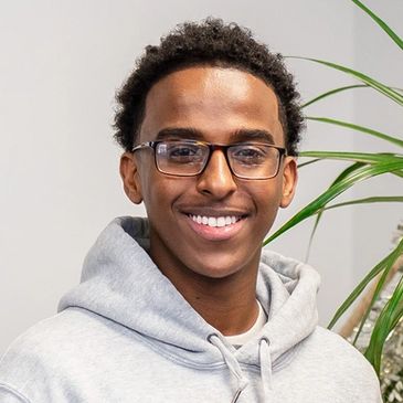 Young man wearing glasses and a gray hoodie smiling.