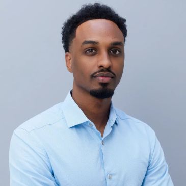 Young man with short curly hair in a light blue shirt.