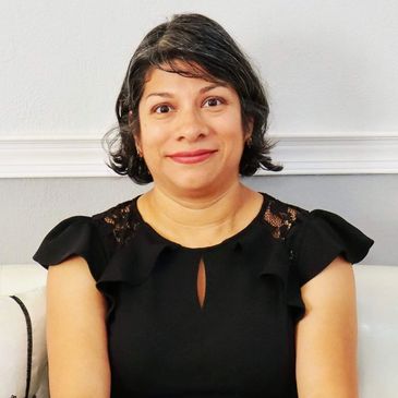 Woman smiling in a black dress with ruffled sleeves indoors.