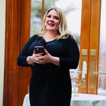 Smiling woman holding a phone indoors near a window.