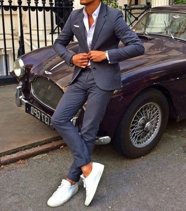 Men's blue grey suit with white dress shirt white hankie white sneakers sitting next to a classic ca