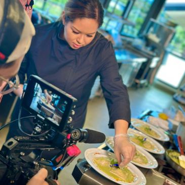 Chef preparing dishes while being filmed in a professional kitchen.