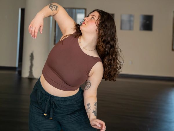 A woman with tattoos poses gracefully in a dance studio.