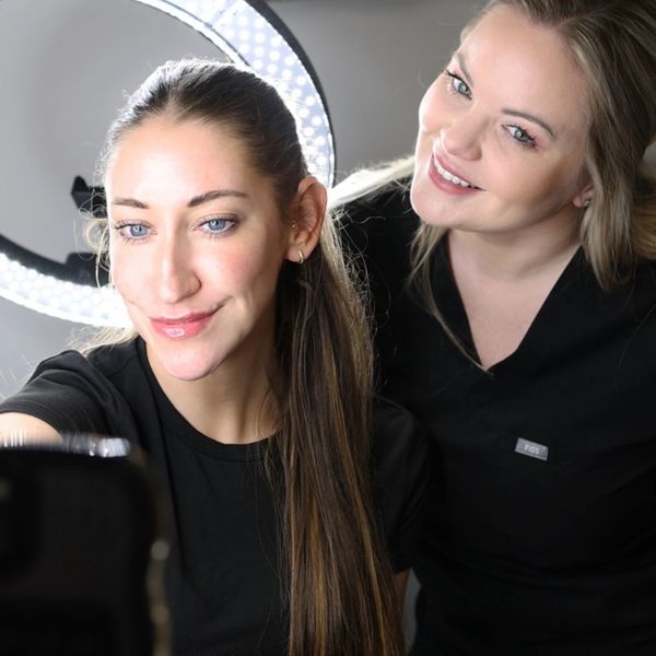 Two women taking a selfie with a ring light behind them.