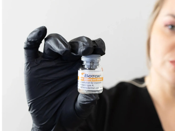 Woman holding a Botox vial wearing black gloves.