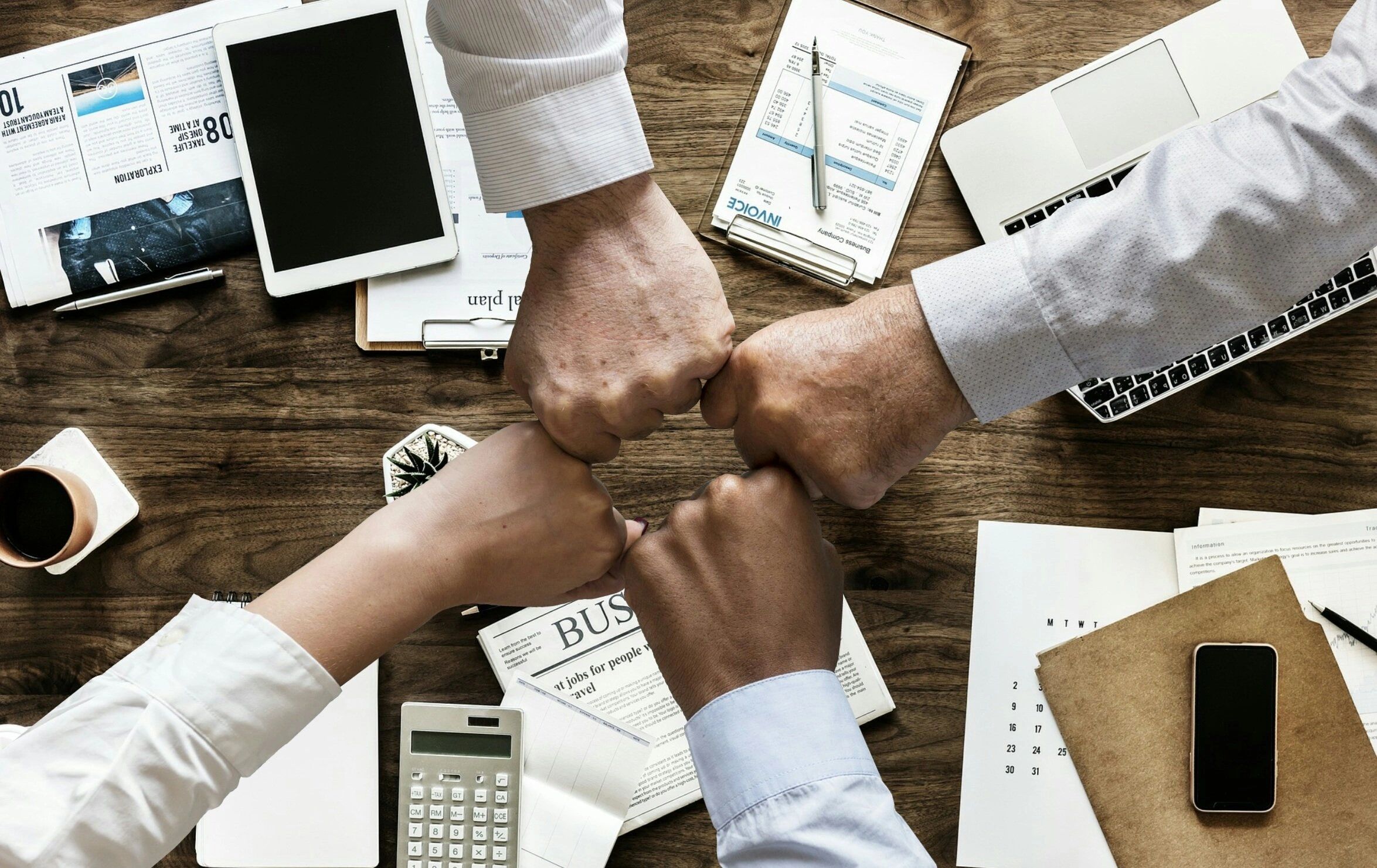 Four people doing a group fist bump over a cluttered desk.