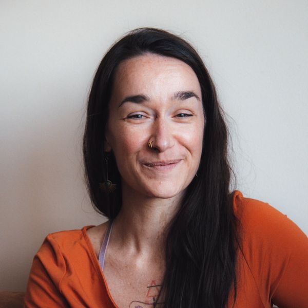 Woman with long dark hair smiling gently in an orange top.