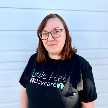 Person wearing a 'Little Feet Daycare' shirt and glasses, smiling.