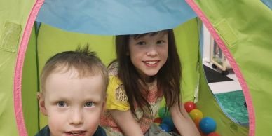 Two children playing in a colorful tent with balls.
