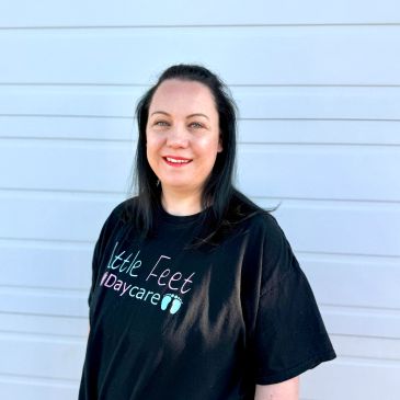 Woman smiling wearing a Little Feet Daycare T-shirt.