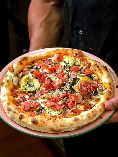 A freshly baked pizza with artichokes, mushrooms, and diced tomatoes.