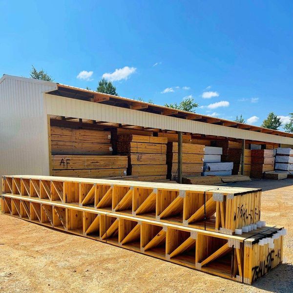 truss at manufacturing plant raw timber in background under metal shed. lumber protected truss built