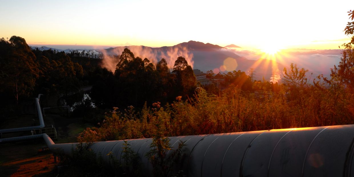 Sunset over misty mountains with industrial pipeline in foreground.