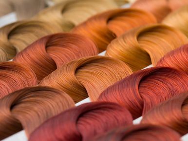 A close-up of a color chart showing rows of hair swatches in shades of blonde, orange, and red.