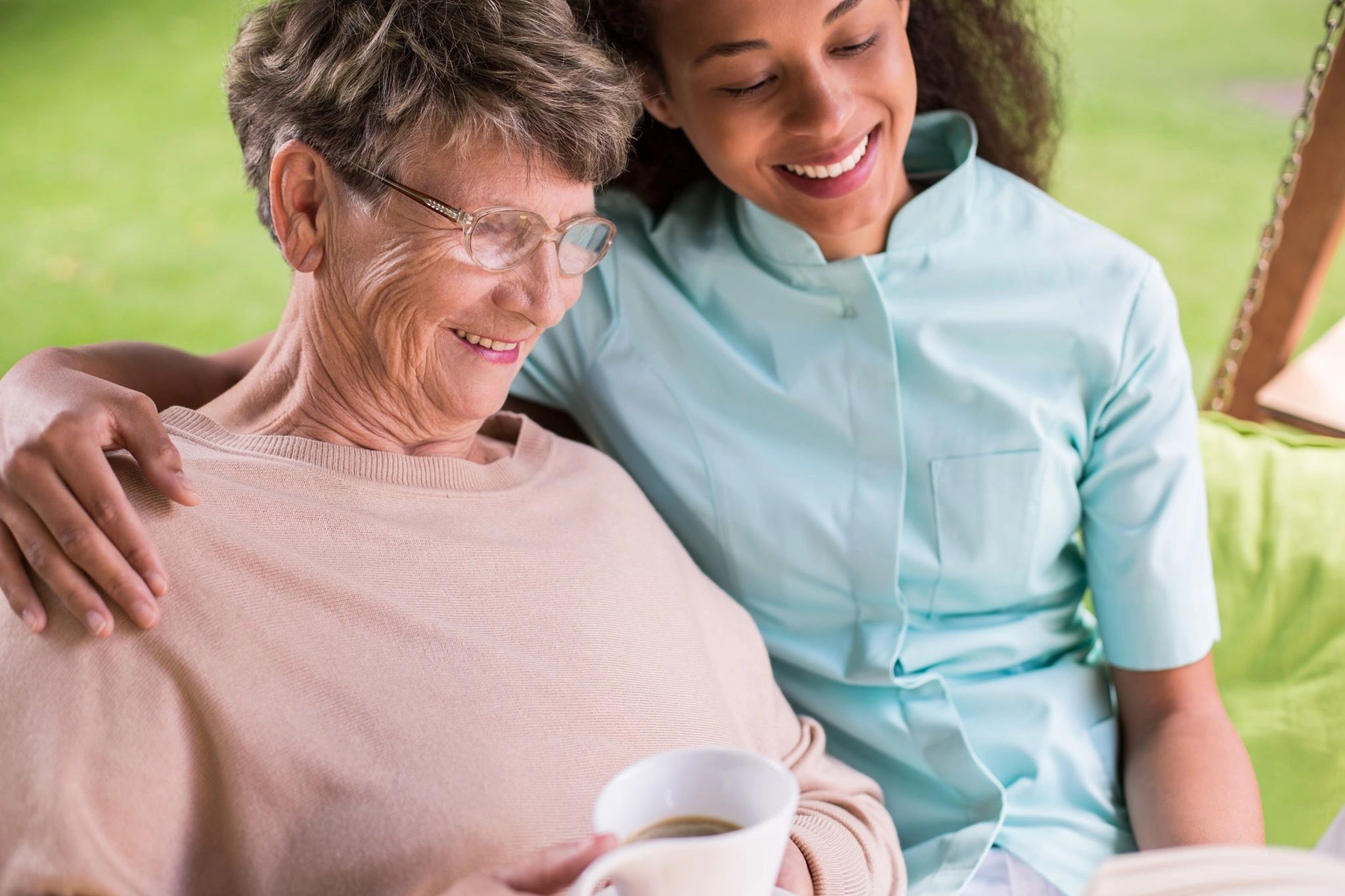 Caregiver and elderly woman smiling and reading together.