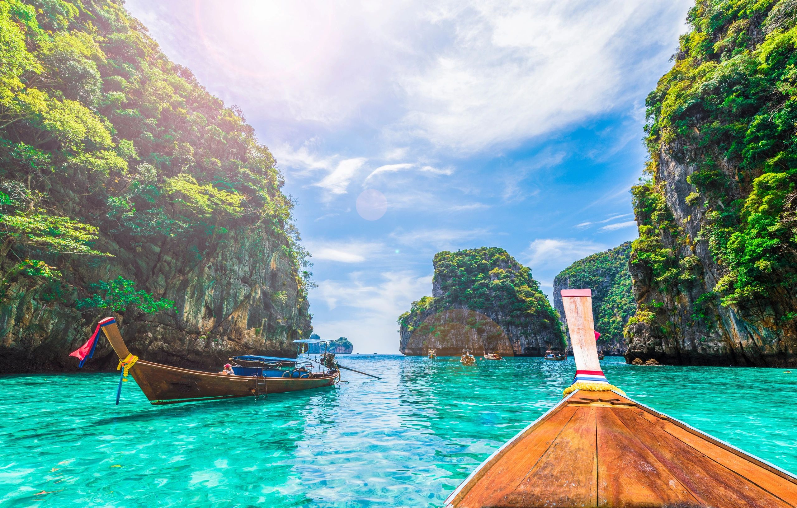 Traditional wooden boat on crystal-clear turquoise waters surrounded by lush cliffs under a blue sky