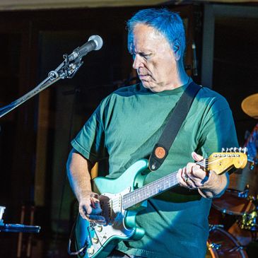 Musician intensely playing electric guitar on stage under blue light.
